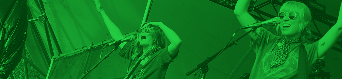 two women sing on stage at a festival with green overlay